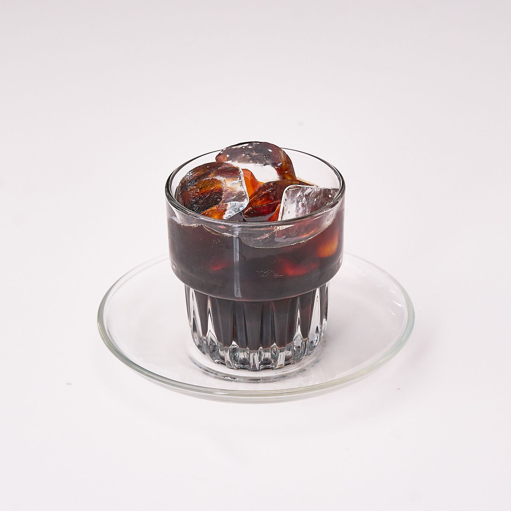 A glass of classic iced black coffee on a saucer.